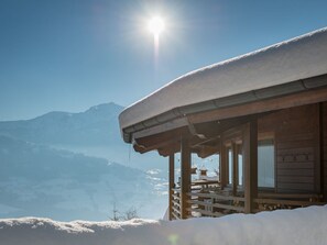 A wooden cabin with a snow-covered roof, wooden railings, and a view of snow-covered mountains in the background. - für 2 Personen ca. 33 m² in Vomp, Tirol (Unterinntal) by Interhome (Vomp)