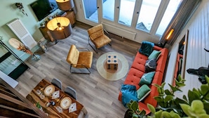 A spacious living area with a sofa, chairs, a dining table set for four, a TV, and a large window with a view of the outside. - Schwarzwald Loft mit Schwimmbad und herrlicher Aussicht by Interhome (Sasbachwalden)