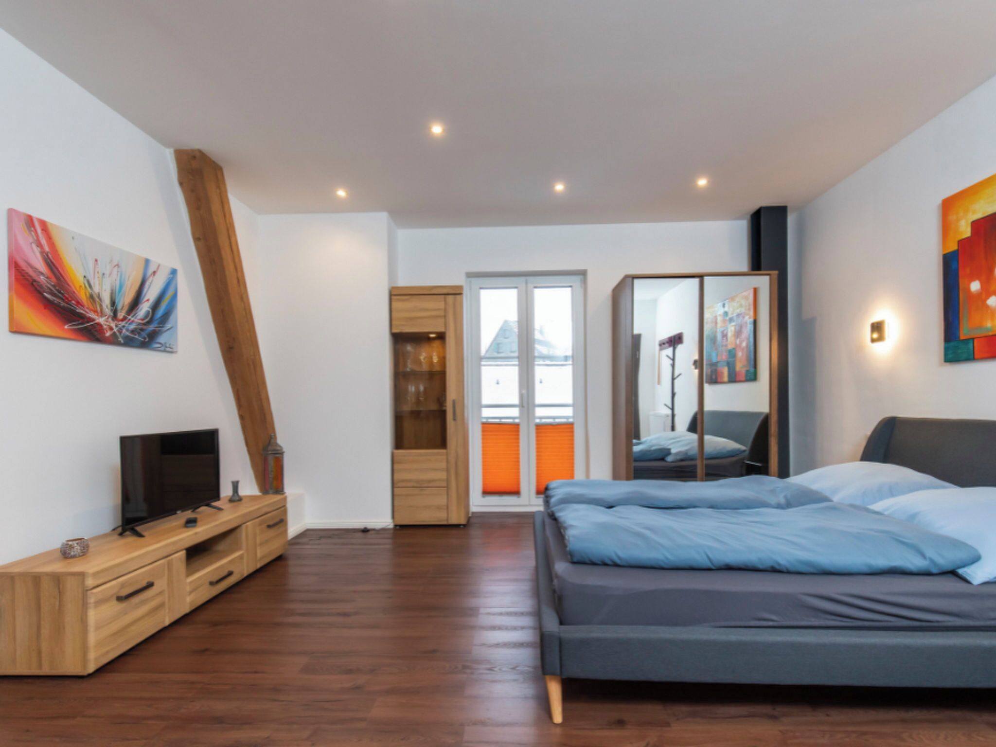 A modern bedroom with a bed, wooden TV stand, and a sliding door leading to a balcony.