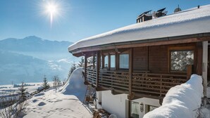 En træchalet med balkon med udsigt over et sneklædt landskab og bjerge.