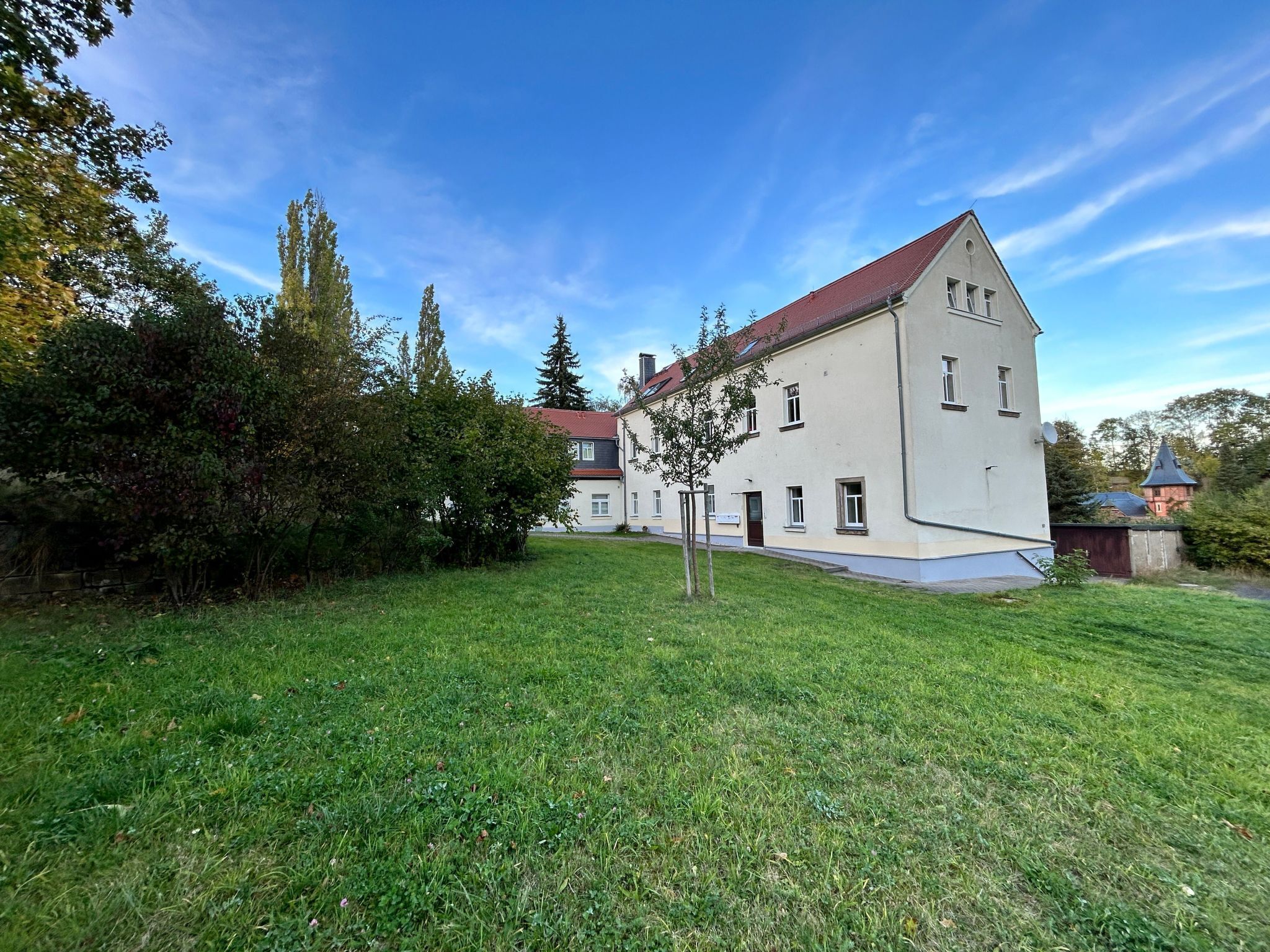 A large, two-story building with a red roof and white walls, surrounded by a well-maintained lawn and trees.
