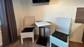Una habitación pequeña con dos sillas de mimbre, una mesa y un televisor de pantalla plana montado en la pared.