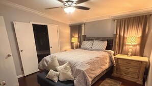 Ein Schlafzimmer mit einem Bett, Nachttischen, einem Deckenventilator und einem Nachtschränkchen.