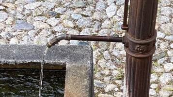 Ein rustikaler Wasserspeier mit einem Steinkessel, vor einer Kulisse aus Kieselsteinen und Grünpflanzen.