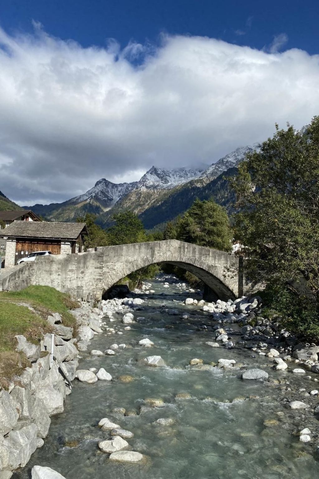 Un pont de pierre enjambe un ruisseau aux eaux claires, avec des montagnes en arrière-plan.