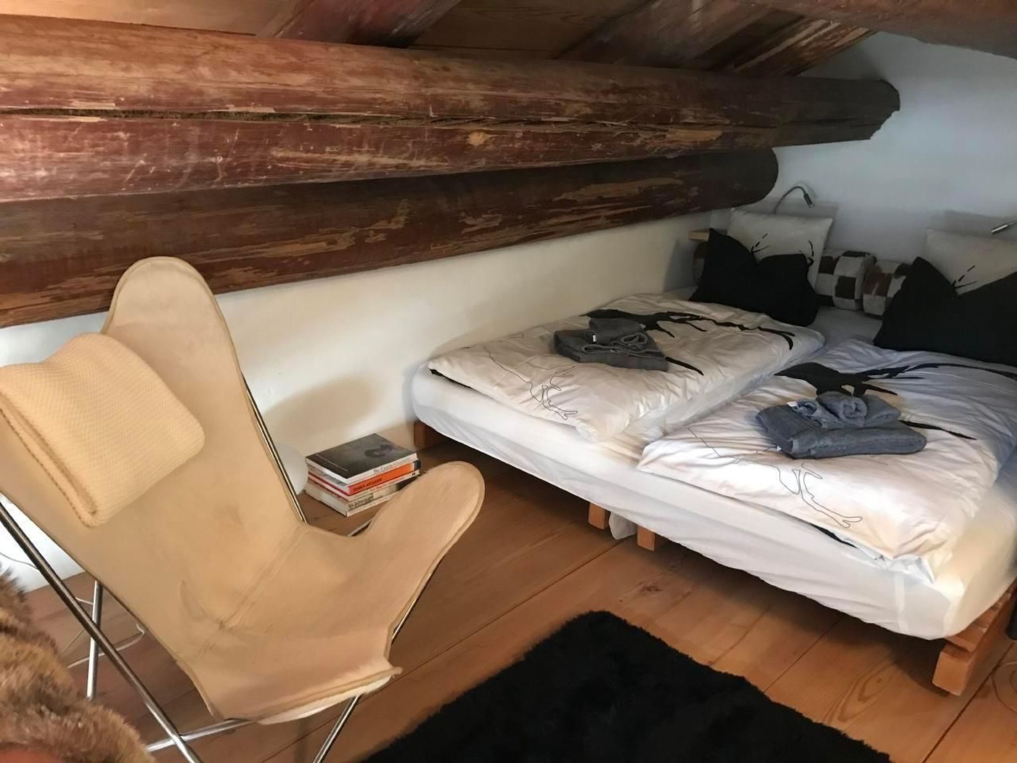 Ein kleiner, gemütlicher Raum mit einem Einzelbett, einem Sessel und einer Holzbalkendecke.