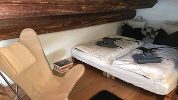 Ein kleiner, gemütlicher Raum mit einem Einzelbett, einem Sessel und einer Holzbalkendecke.