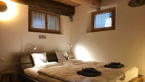 Un dormitorio acogedor con una cama de madera, dos lámparas de noche, un taburete pequeño y dos ventanas con cortinas.