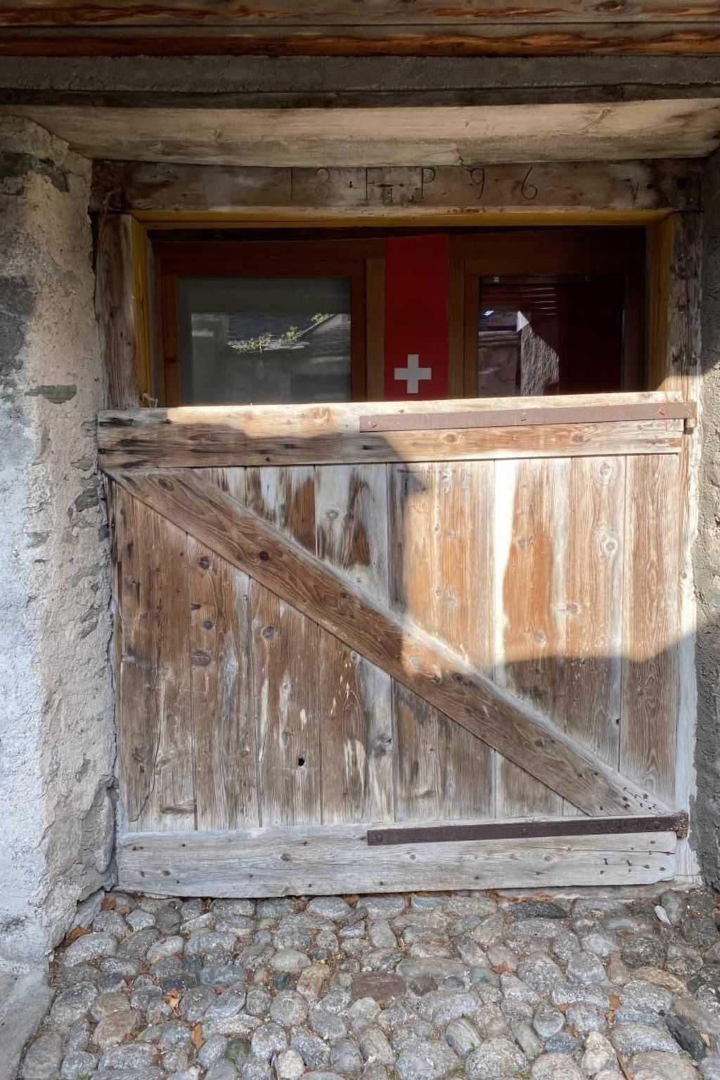 Eine rustikale Holzhütte mit Steinunterbau, einer Holztür mit einem roten Kreuz und einem Fenster mit Landschaftsblick.