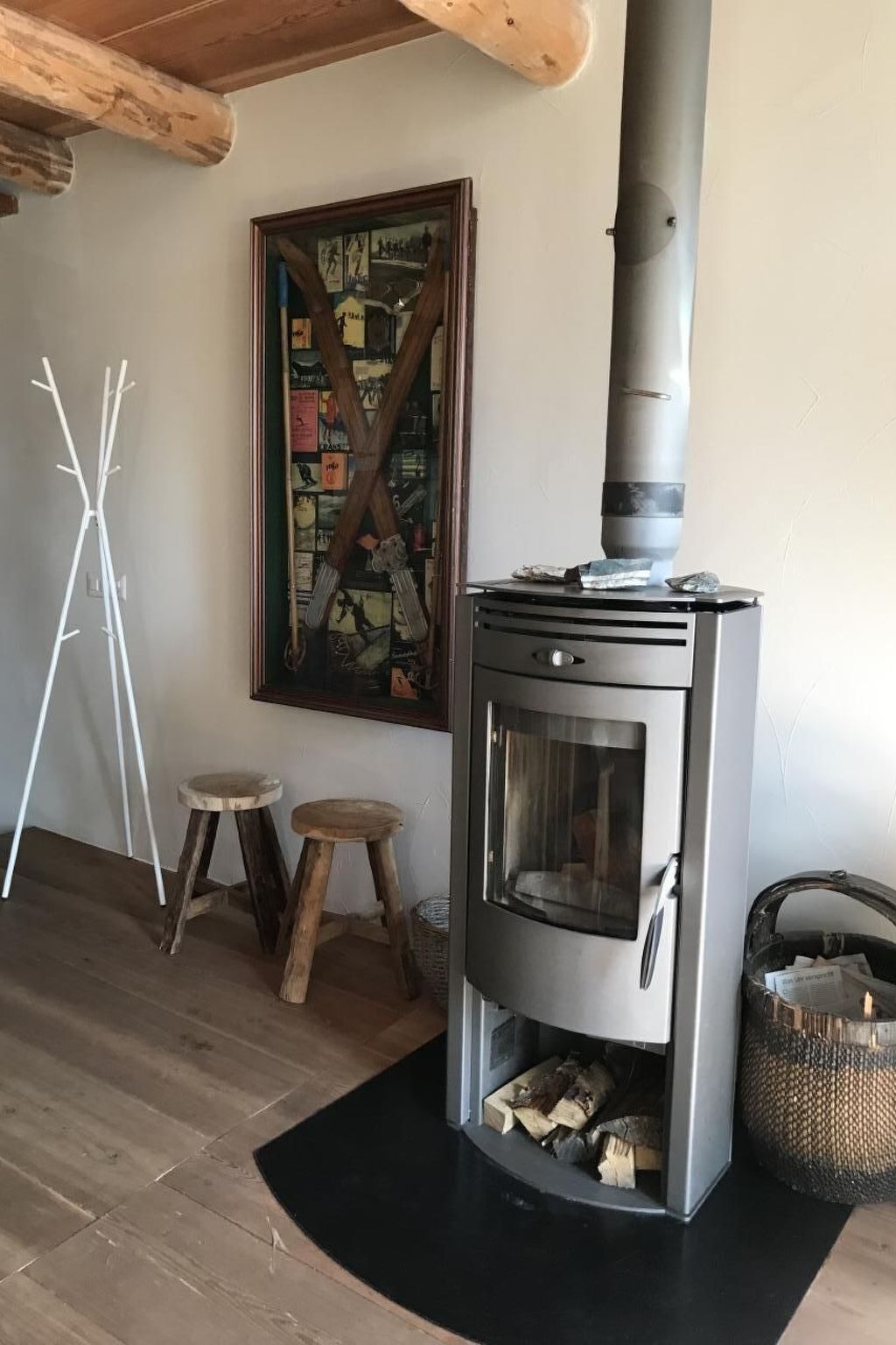 Ein Zimmer mit Kaminofen, einem gerahmten Gemälde, zwei Hocker und einem gewebten Korb.