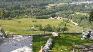 A mountainous landscape with a village, a power line tower, and a fenced area with logs. - Casa Tavernela by Interhome (Vicosoprano)