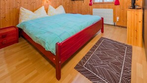 A wooden-paneled bedroom with a bed, a nightstand, a bookshelf, a radiator, and a window with curtains. - Casa Tavernela by Interhome (Vicosoprano)