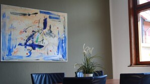 A dining area with a table and chairs, a large abstract painting on the wall, and a window with a view of the outside. - Gemütliche Wohnung in Wernigerode mit Garten by Interhome (Wernigerode)