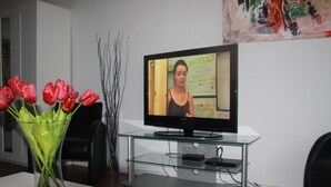 A modern living room with a flat-screen TV on a glass table, a vase of red tulips, and a painting on the wall. - Gemütliche Wohnung in Wernigerode mit Garten by Interhome (Wernigerode)