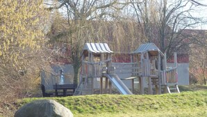 Ein Spielplatz mit Rutsche und Klettergerüsten, umgeben von Bäumen und einer Rasenfläche.