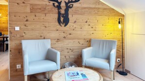 A room with two light blue chairs, a round woven coffee table with magazines, and a wooden wall with a deer head decoration. - FeWO Allgäu Chalet - gemütliche Hüttenatmosphäre und Schwimmbad und Sauna im Ha by Interhome (Oberstdorf)