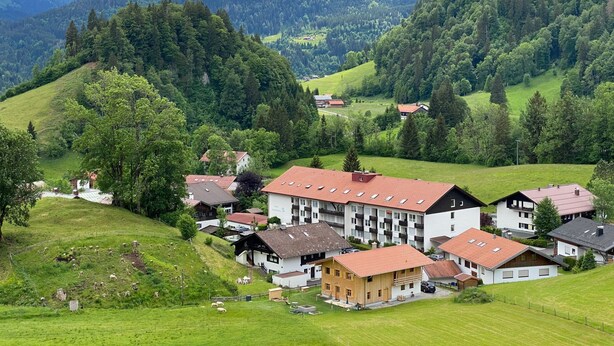 A rural village with traditional houses, a central building with a red roof, and surrounding green hills. - FeWO Allgäu Chalet - gemütliche Hüttenatmosphäre und Schwimmbad und Sauna im Ha by Interhome (Oberstdorf)