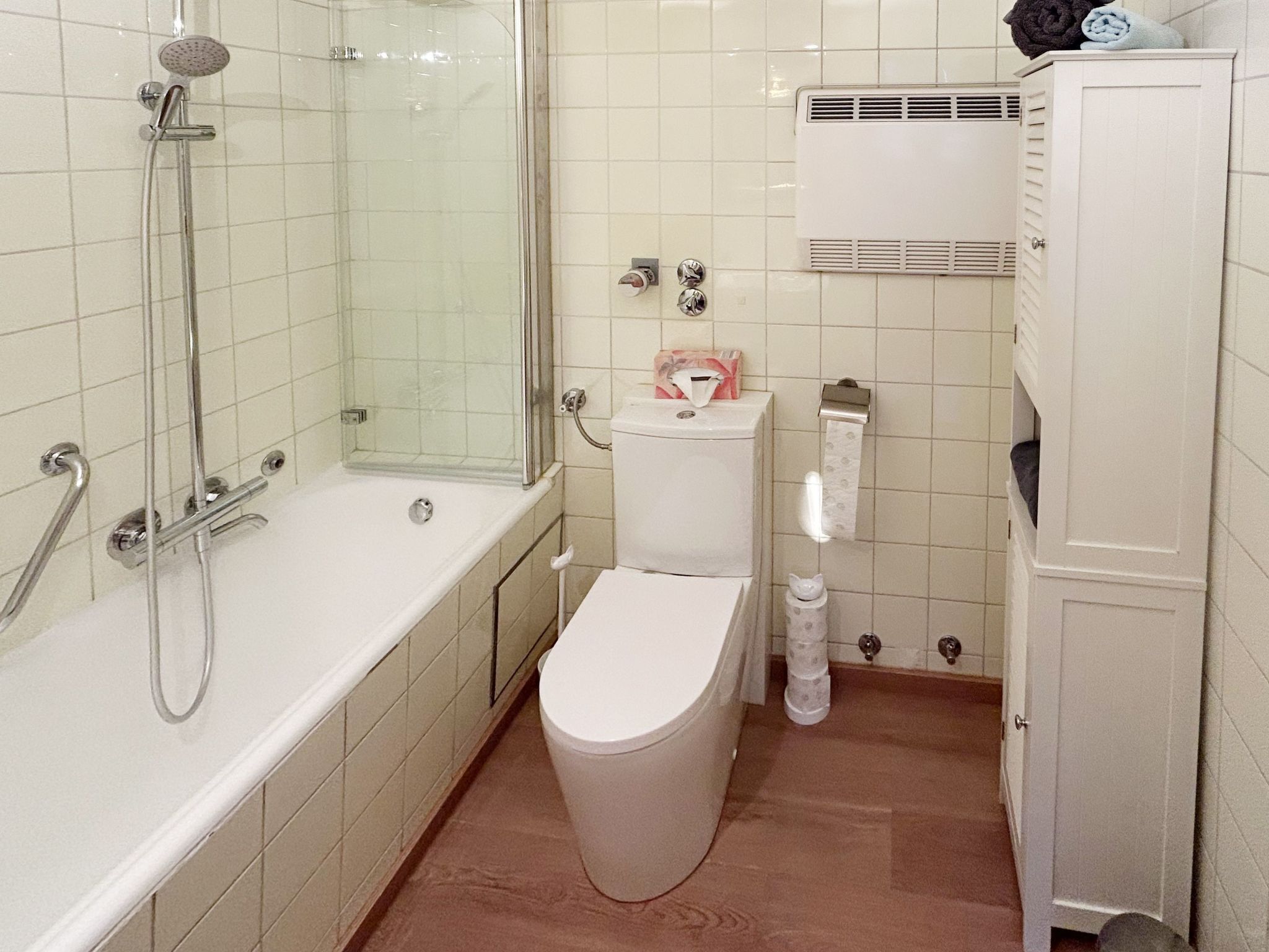 Kylpyhuoneessa on lasiseinällä varustettu suihku, valkoinen wc-istuin ja valkoinen kaappi, jossa on pyyhkeitä.