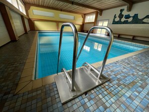 Ein Innenpool mit gefliesten Wänden und einer Holzbalkendecke.