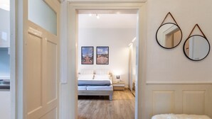 Une chambre avec un plancher en bois, un lit, une table de chevet, deux tableaux encadrés et un banc blanc moelleux.