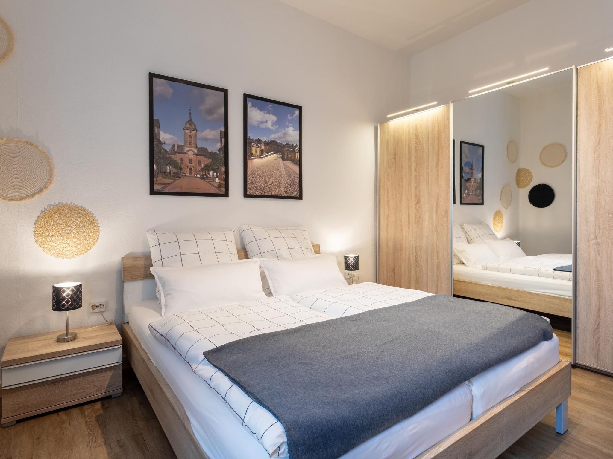 A modern bedroom with a large bed, a nightstand, a mirror, and two framed pictures on the wall.