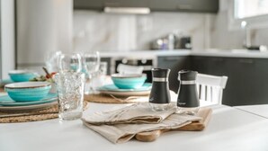A kitchen with a table set for dining, featuring clear glassware, turquoise plates, and black condiment bottles.