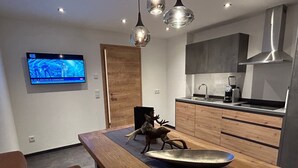 Eine moderne Küche mit Holzschränken, einer Edelstahl-Spüle und einem eingebauten Backofen. An der Wand ist ein großer Flachbildfernseher angebracht und auf dem Esstisch steht eine dekorative Hirschskulptur.
