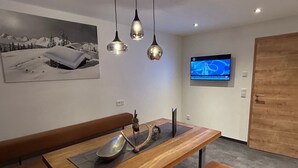 Ein moderner Essbereich mit Holztisch, Sitzbänken, Pendelleuchten und einem an der Wand befestigten Fernseher.