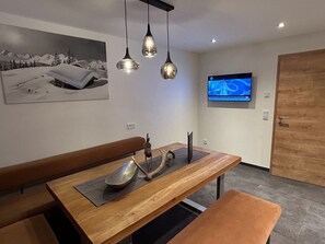 Ein moderner Essbereich mit Holztisch, Sitzbänken, Pendelleuchten und einem an der Wand befestigten Fernseher.