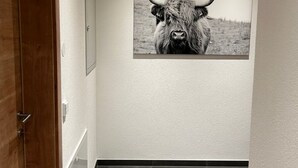 Ein Flur mit Holztür, einem gerahmten Bild eines Stiers, Einbuchtungslampen und grauen Fliesenböden.
