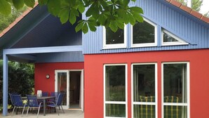 Une maison à l’extérieur rouge, avec un toit bleu et une terrasse couverte comprenant une table et des chaises.
