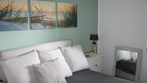 Une chambre à coucher avec un lit, des oreillers, une table de chevet, une lampe et un tableau encadré au mur.