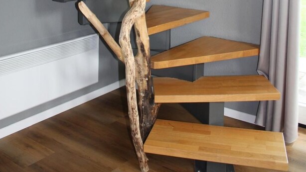 Un escalier au design original en bois, des murs gris et une fenêtre avec des rideaux.