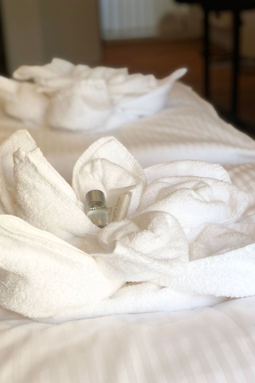 Ein ordentlich bezogenes Bett mit Lotionflasche und einem gefalteten Handtuch.