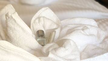 Ein ordentlich bezogenes Bett mit Lotionflasche und einem gefalteten Handtuch.