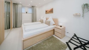 Ein modernes Schlafzimmer mit einem großen Bett, Nachttischen, einem Spiegel und Blick ins Freie.