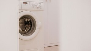 Eine weiße Waschmaschine im Vordergrund, in einem Raum mit weißen Schränken.