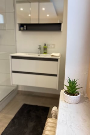 Ein modernes Badezimmer mit einem weißen Waschtisch, einem kleinen Topfpflanzen und einem schwarzen Teppich.