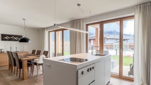A modern kitchen with a central island, a dining area with chairs, and large windows offering a view of the outdoors. - Luxus Chalet Poolblick - mit eigener Sauna by Interhome (Seefeld in Tirol)