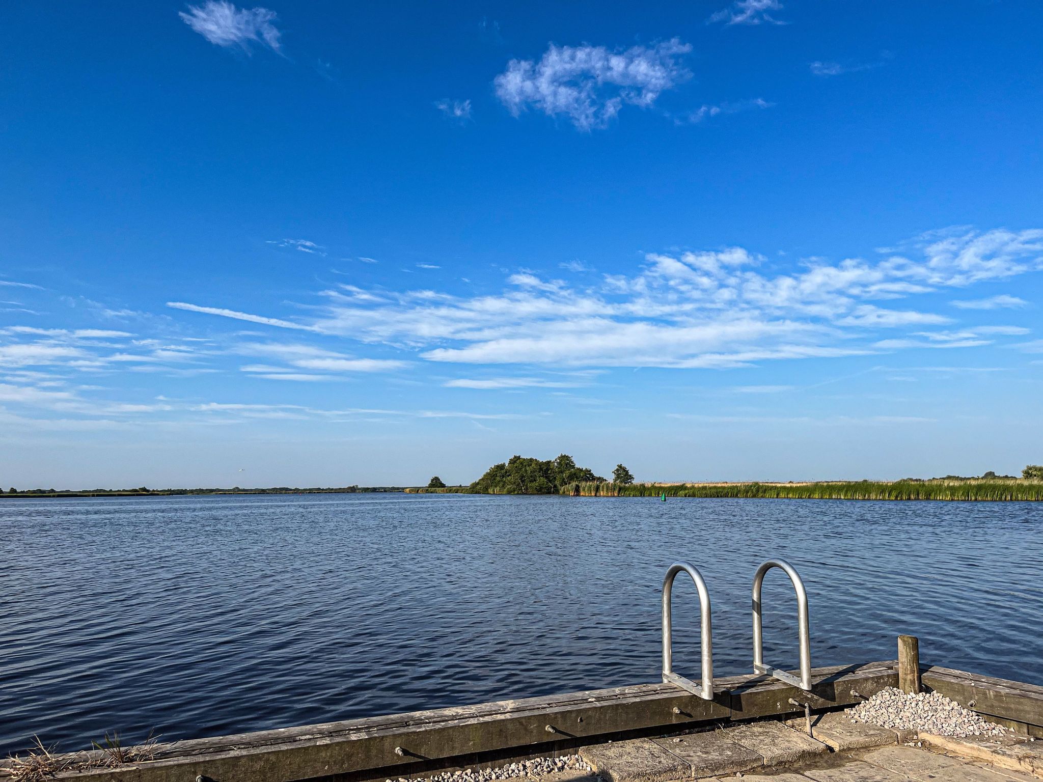 Un lac paisible, avec un quai et des garde-corps en métal.