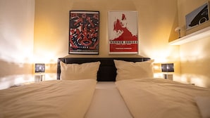 Une chambre d’hôtel avec deux lits, une grande affiche au mur et une lampe de chaque côté du lit.