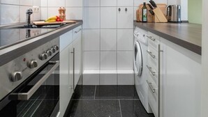 Une cuisine compacte avec des meubles blancs, une cuisinière noire, un lave-linge et un mur d’accent rouge.