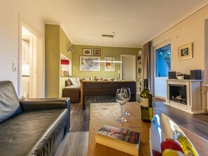 A cozy living room with a leather sofa, a wooden coffee table, and a fireplace. There is a dining area with a wicker table and chairs, and a kitchen in the background. - Hexenzauber Hahnenklee by Interhome (Goslar)