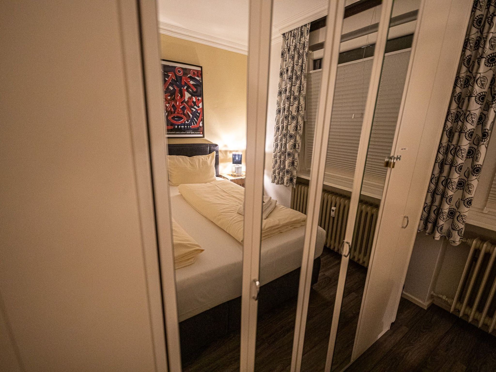 Ein Schlafzimmer mit Bett, Nachttisch, Heizkörper und einer Tür zu einem Schrank.