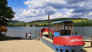A boat named 'MS Diamant' on a sandy beach by a lake with a backdrop of green hills and a partly cloudy sky. - für 6 Personen ca. 60 m² in Diemelsee-Heringhausen, Hessen (Hessisches Ber by Interhome (Diemelsee)