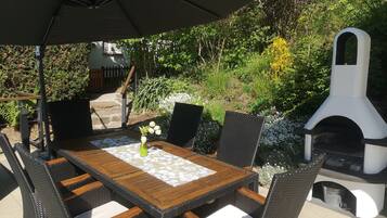 Eine Außenpatio mit einem Holztisch und Korbstühlen, einem Grill und einer Steintreppe.