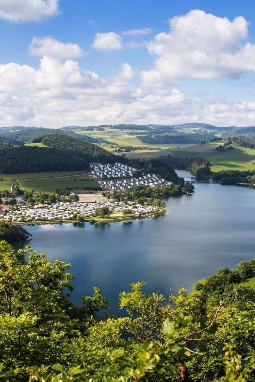 A lakeside campground with RVs and cabins, surrounded by hills and greenery.