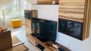 A modern living room with a large flat-screen TV, wooden cabinetry, and a bright yellow ottoman. - Villa Specht- Ferienbungalow by Interhome (Neubukow)