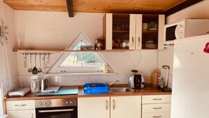A compact kitchen with a window, wooden cabinets, a stove, and a microwave. - Villa Specht- Ferienbungalow by Interhome (Neubukow)