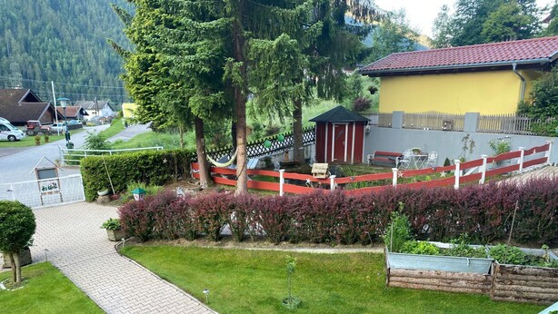 A residential area with a paved driveway, a small red and white fence, and a yellow building with a red roof. - Appartement Wasserfall by Interhome (Stall)